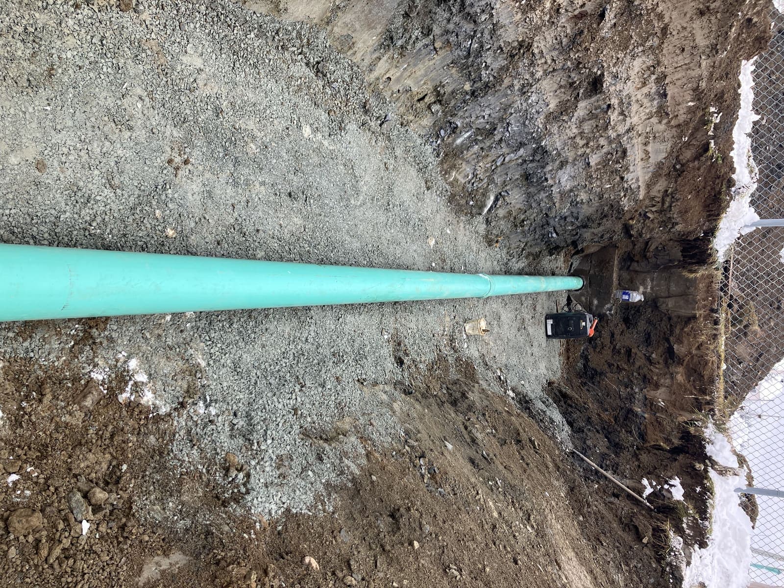 Pose d'une grosse conduite de drainage verte dans une tranchée profonde compactée à Adstock