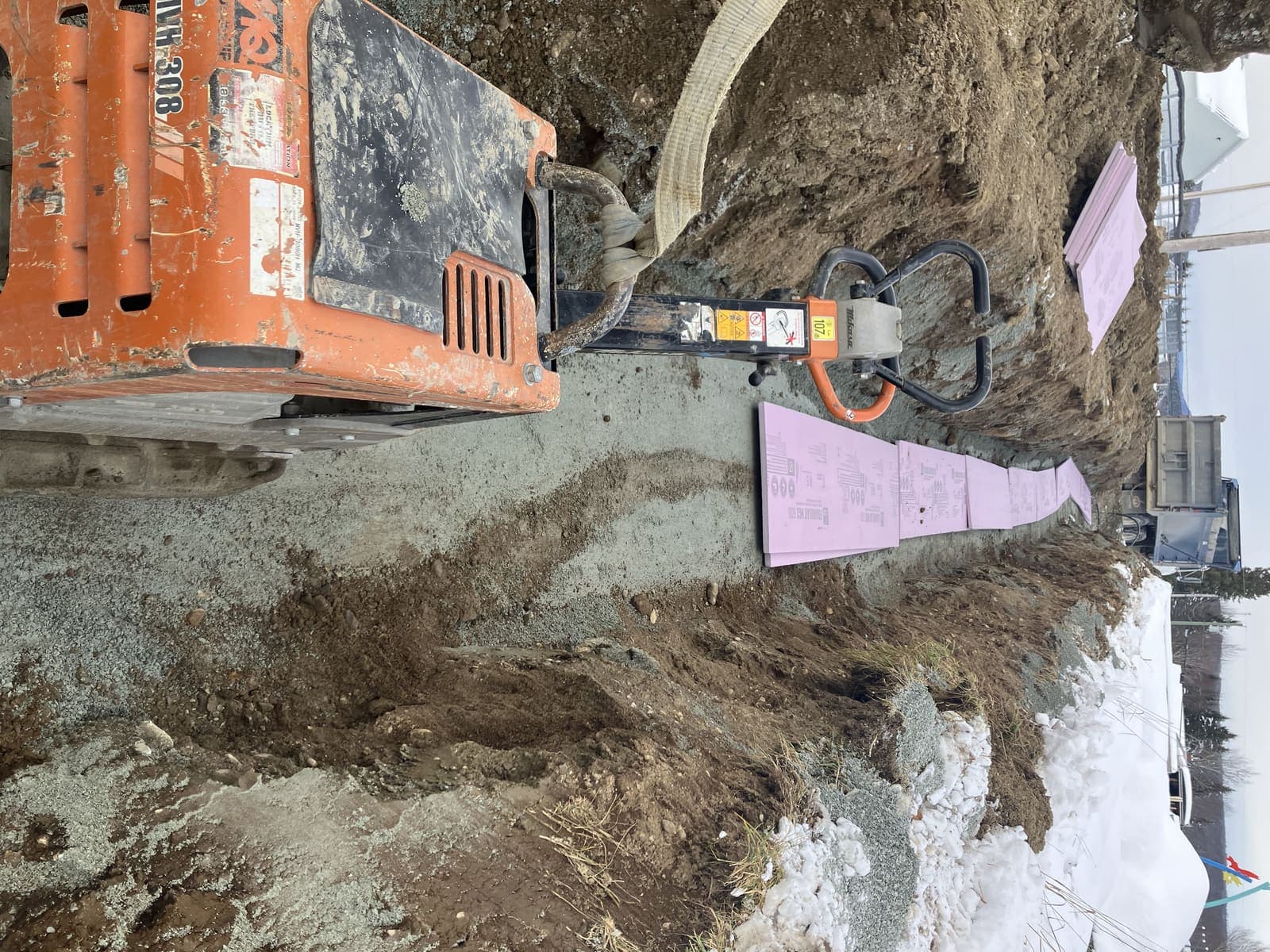 Compacteur orange dans une longue tranchée de drainage avec panneaux d'isolant rose