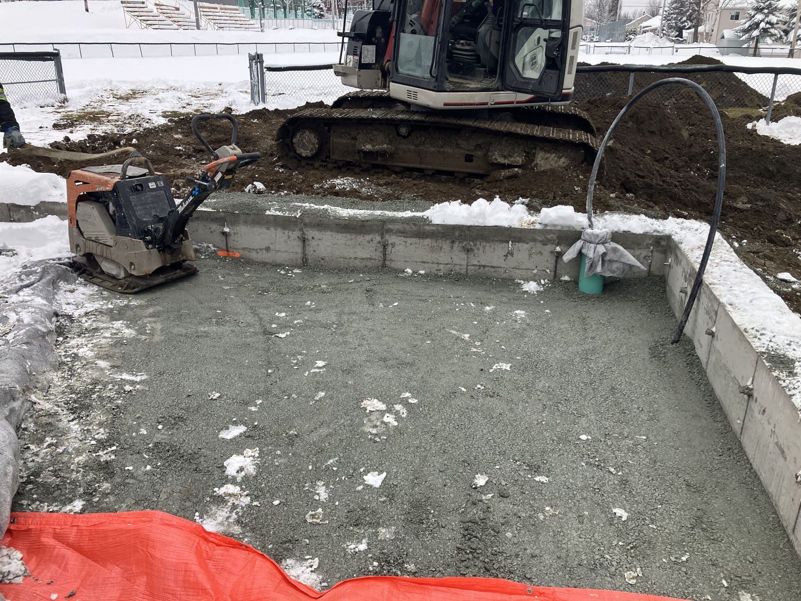 Compactage d'un lit de gravier en bordure d'une fondation avec mini-pelle en hiver