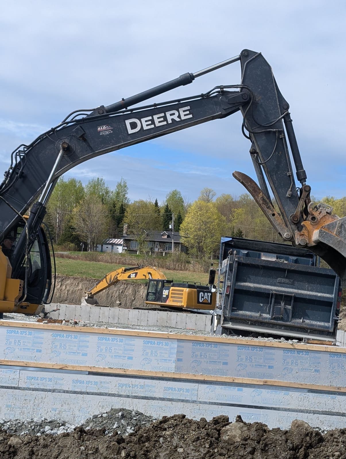 Pelle hydraulique chargeant un camion benne sur un chantier de fondation avec panneaux d'isolant rigide bleu