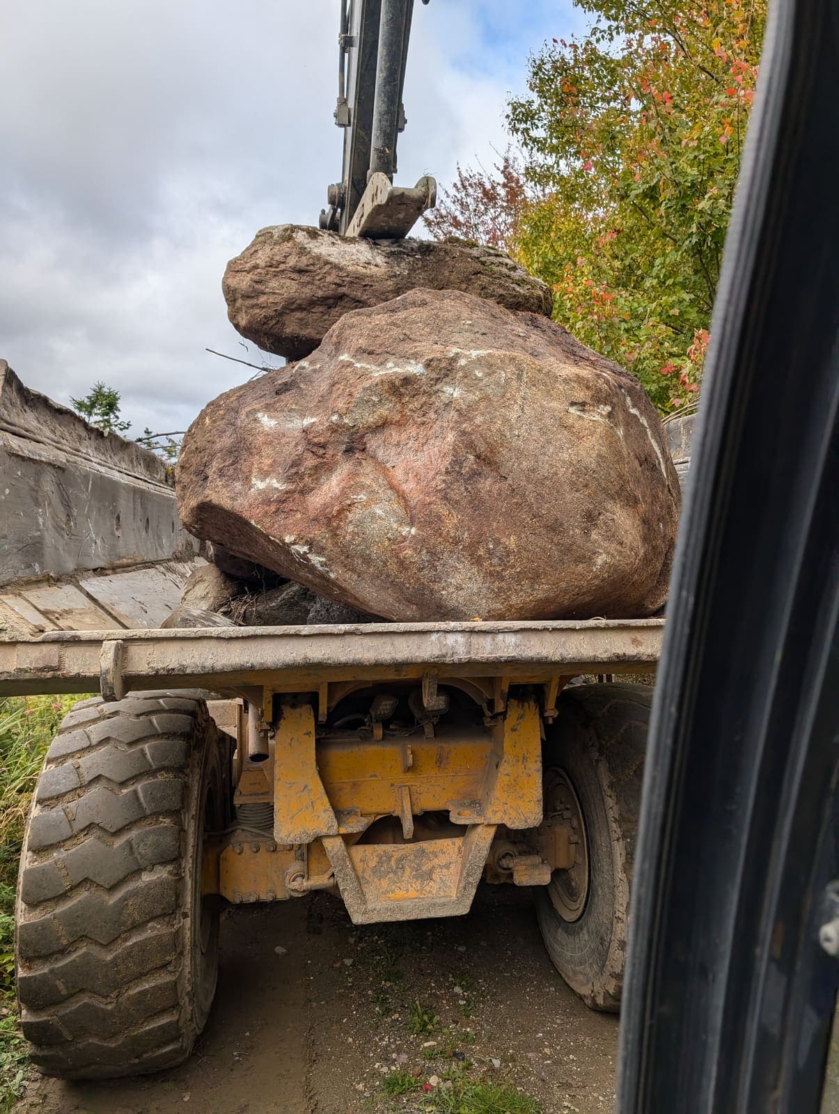 Pelle hydraulique chargeant un gros bloc de roc rouge sur la plateforme d'un tombereau articulé