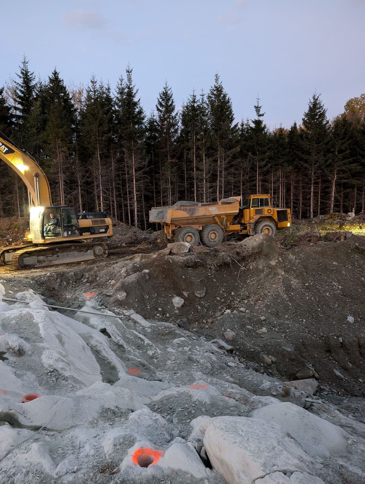Pelle hydraulique et tombereau articulé en opération dans une fosse de roc dynamité, en fin de journée