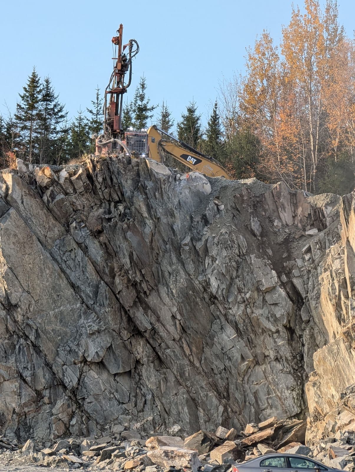 Foreuse chenillée perchée au sommet de la paroi rocheuse pour préparation au dynamitage