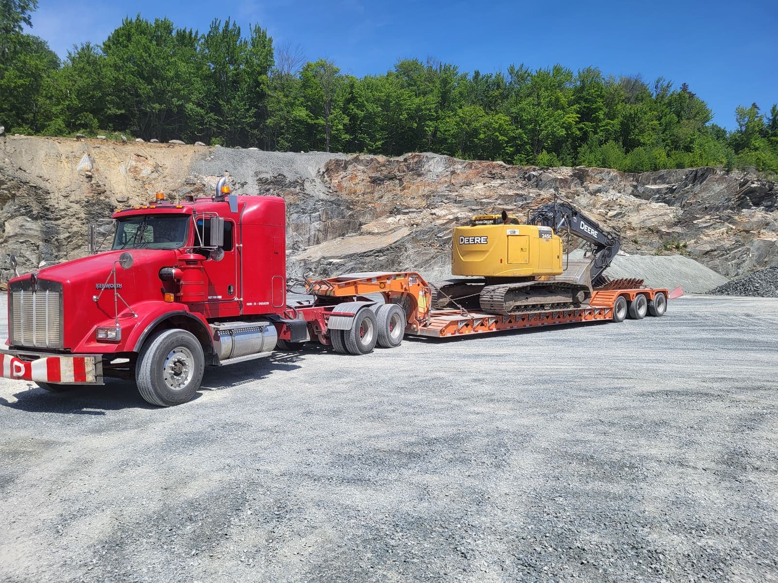 Camion fardier transportant une pelle hydraulique sur le site de la carrière, devant la paroi rocheuse