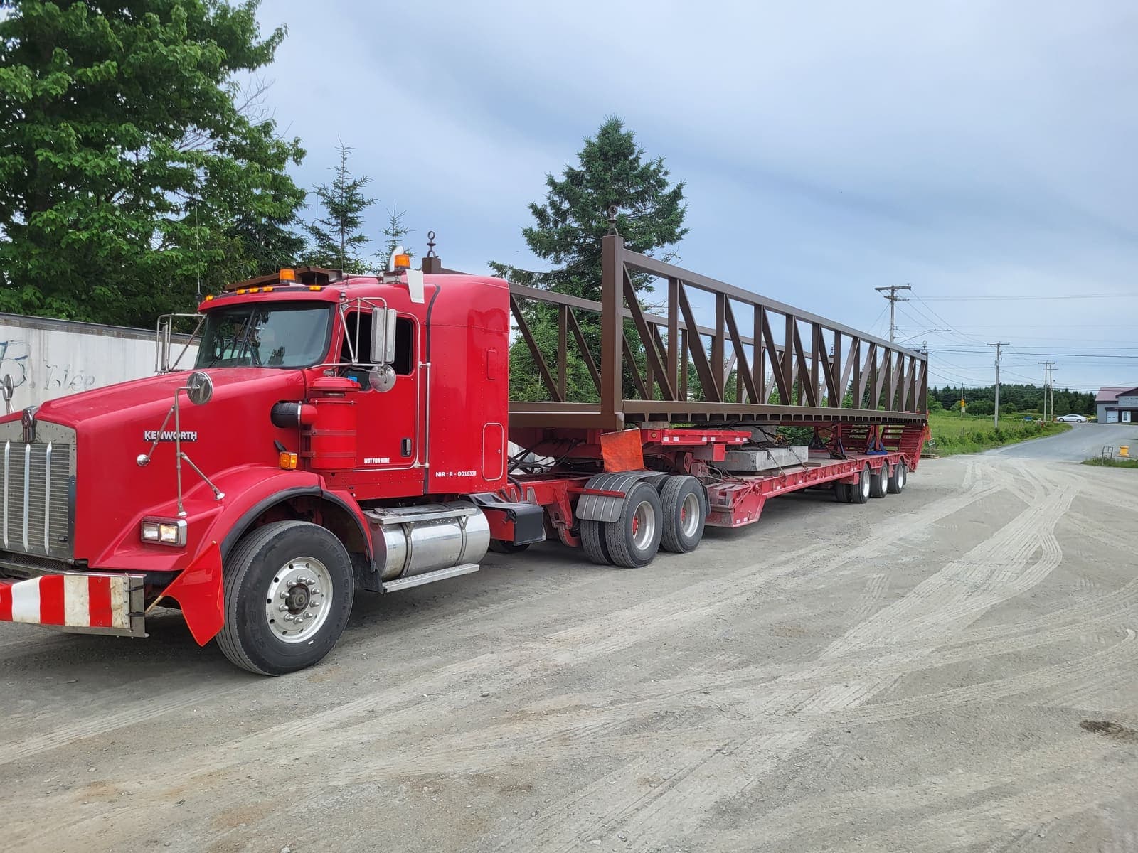Camion fardier extensible transportant une longue structure métallique en treillis