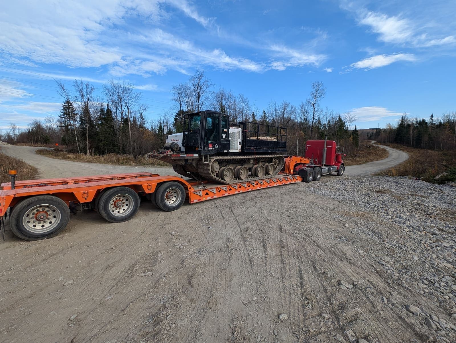 Camion fardier transportant un véhicule chenillé spécialisé sur un chemin de gravier en automne