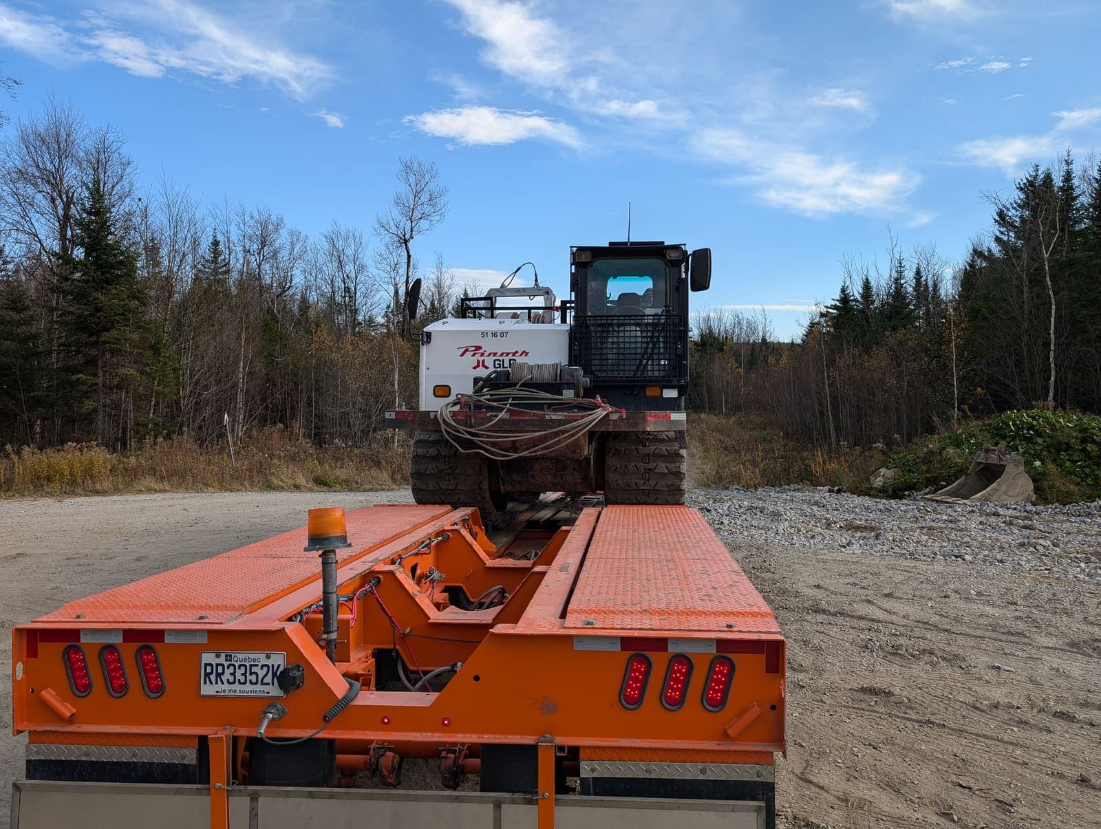 Vue arrière du fardier orange avec véhicule chenillé chargé, prêt à partir