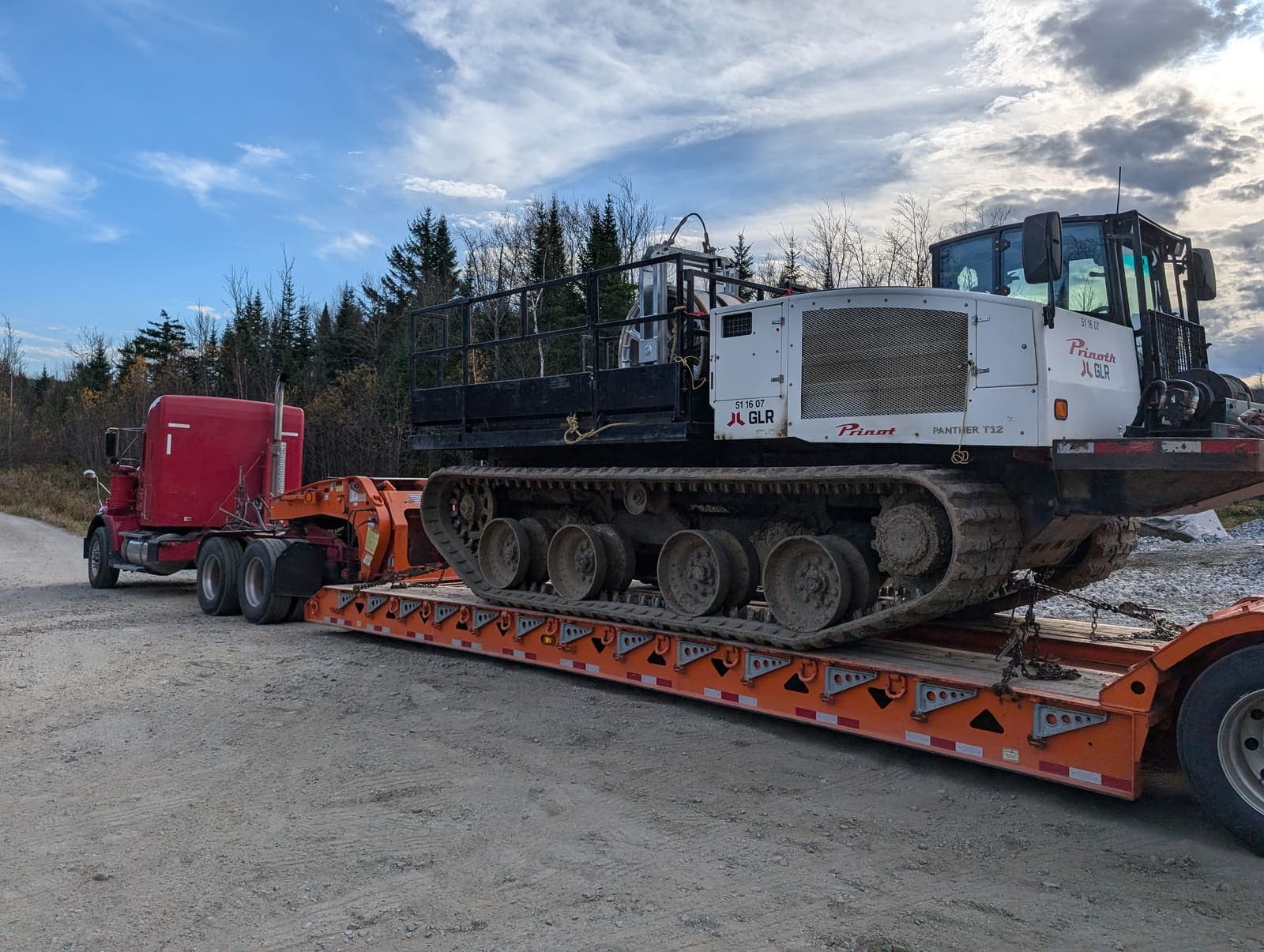 Véhicule chenillé spécialisé attaché sur fardier orange, prêt au transport