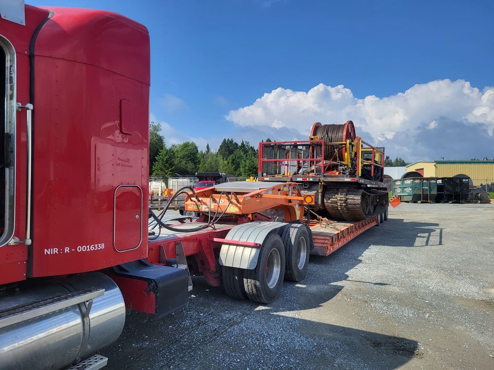 Camion fardier transportant un véhicule chenillé orange équipé de bobines de câble rouges