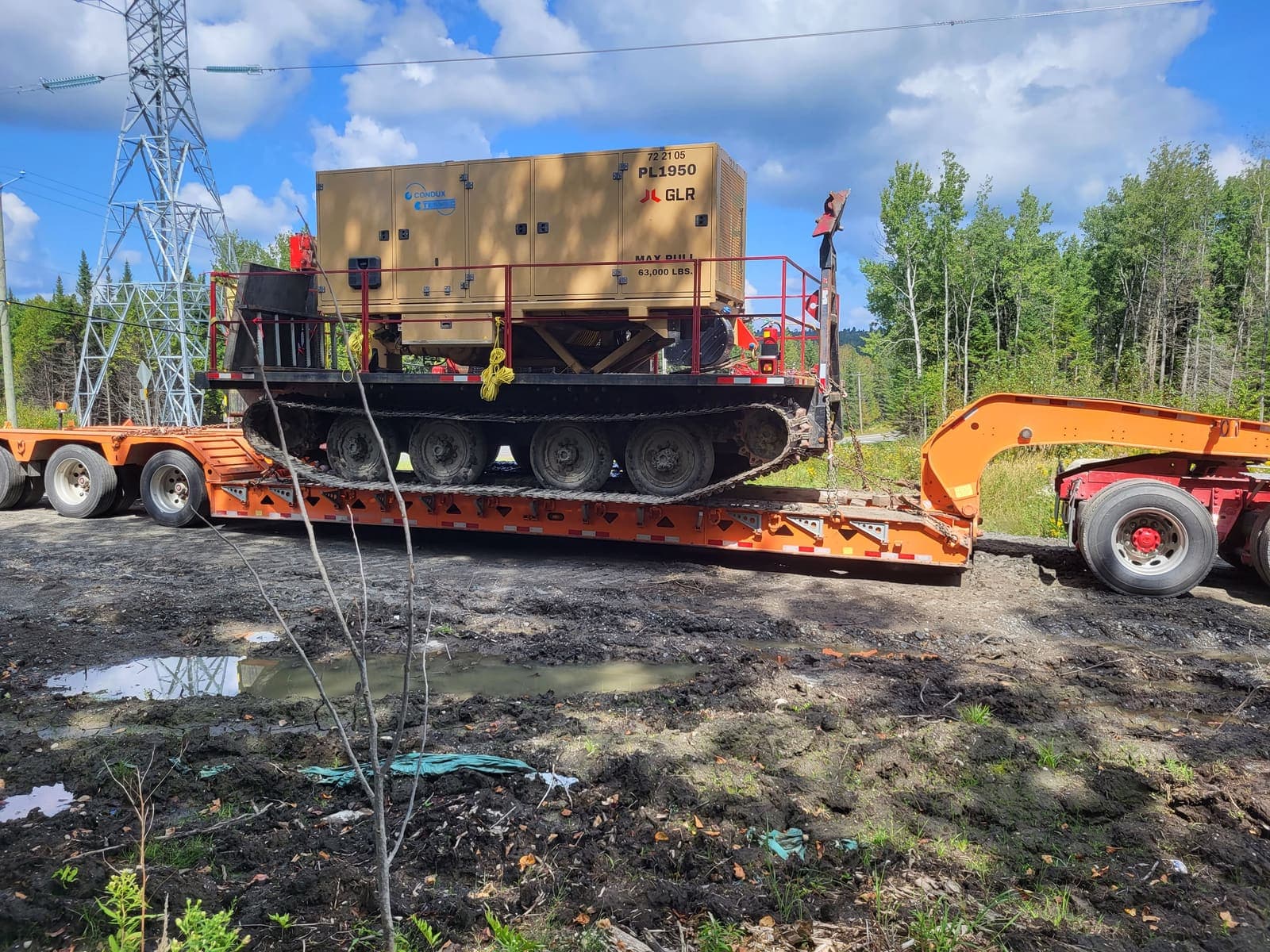 Véhicule chenillé orange transportant une génératrice industrielle, sur fardier en bordure de chantier