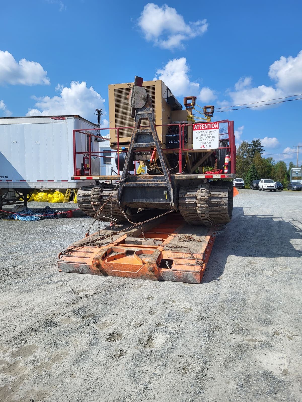 Vue arrière d'un véhicule chenillé spécialisé avec sa rampe de chargement déployée sur fardier
