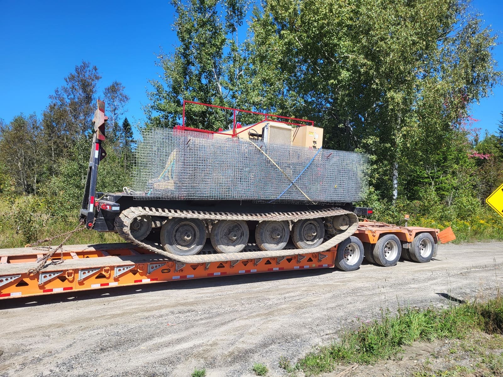 Véhicule chenillé blindé chargé sur fardier orange, en bordure de route
