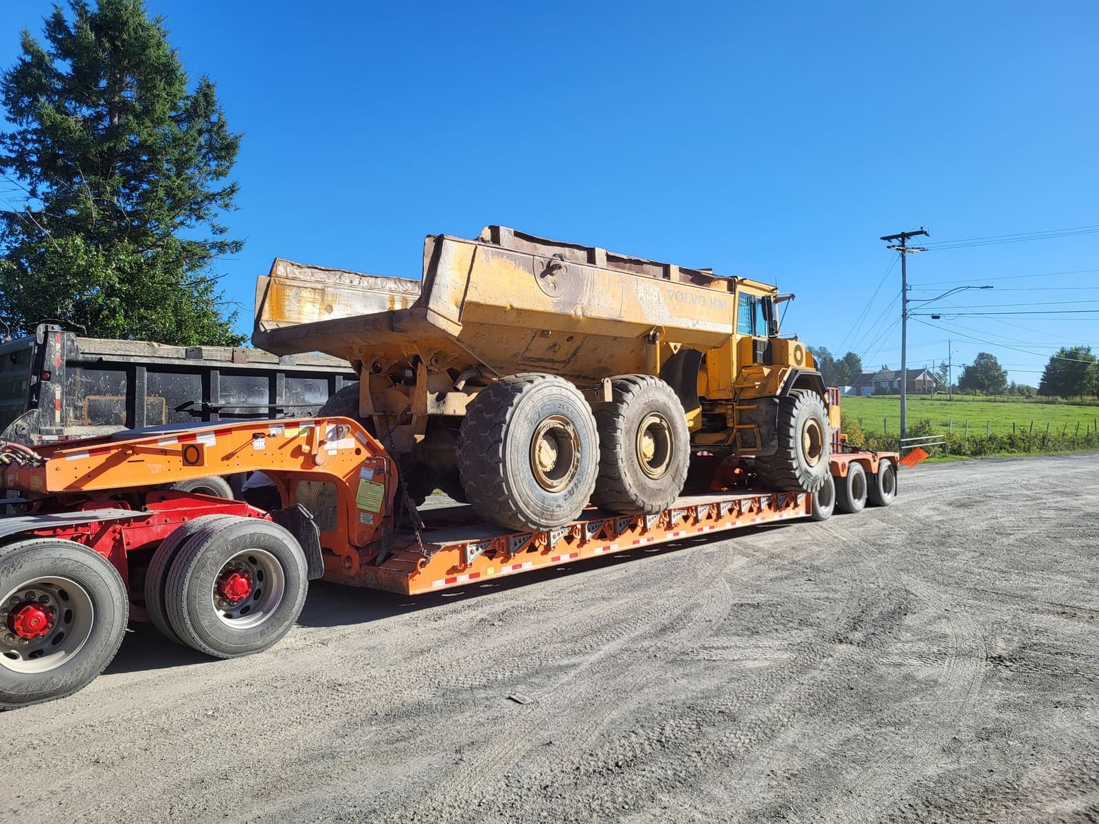 Gros tombereau articulé chargé sur fardier orange, prêt au transport