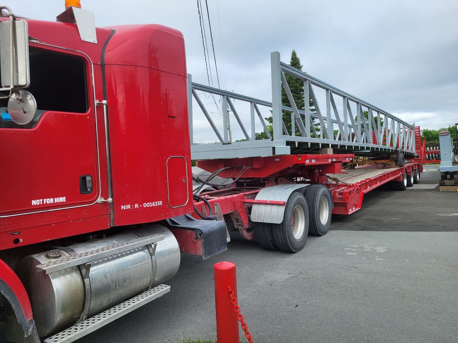 Camion fardier transportant une longue charpente métallique grise en treillis