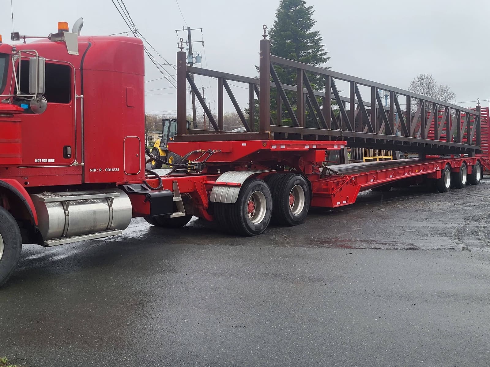 Camion fardier transportant une longue charpente métallique brune sous la pluie