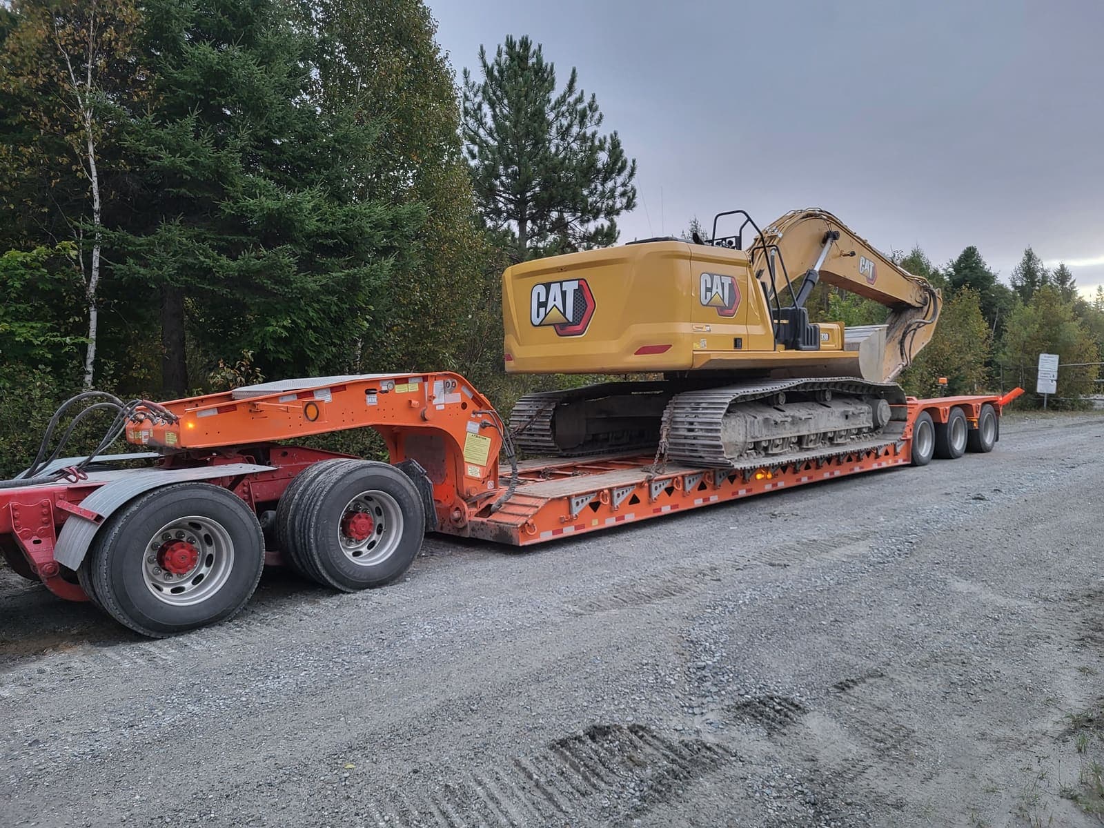 Camion fardier transportant une pelle hydraulique sur chenilles le long d'un chemin forestier